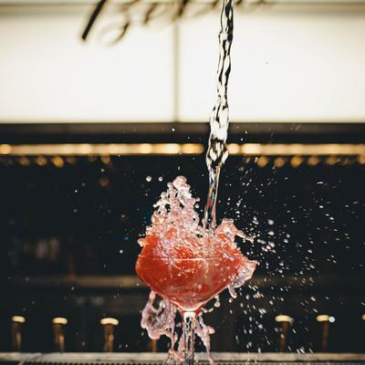 A drink is being poured into a red drink glass on a bar counter, creating a splash.