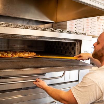 A cook baking a pizza in an oven.