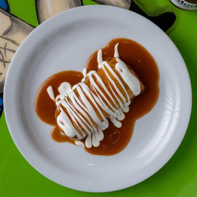 Burrito topped with sour cream and sauce on a white plate.