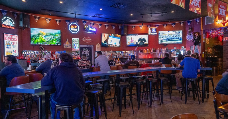 Interior, bar, bartender, tv screens, bar table in front, bar stools, guests