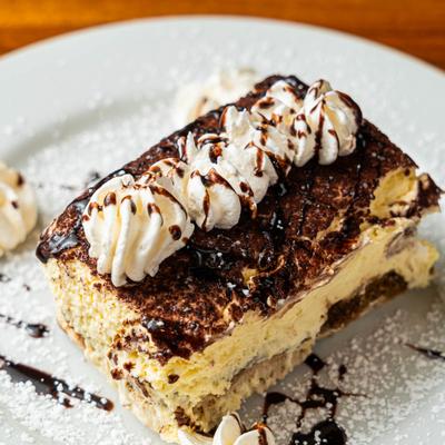 A slice of tiramisu topped with whipped cream and chocolate sauce.