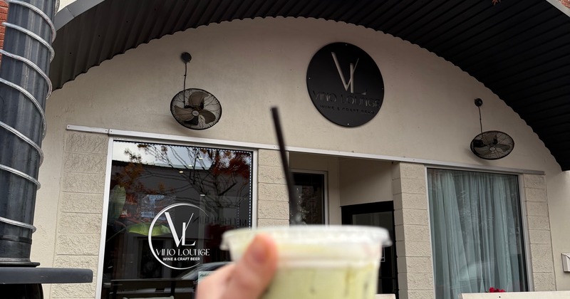 The exterior of Vino Lunge, a drink in a clear cup is being held in the foreground