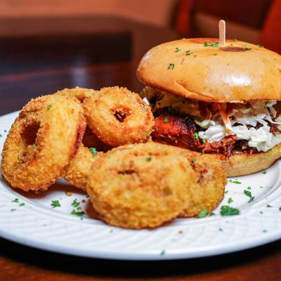 Pulled pork sandwich served with fried onion rings.
