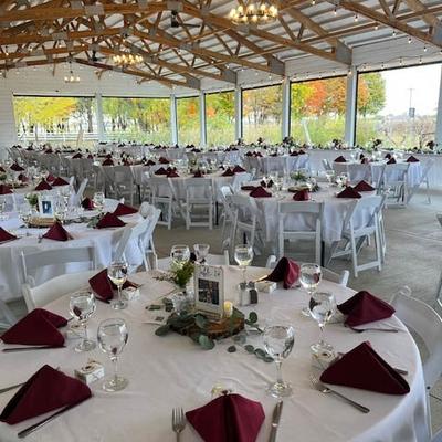 Spacious outdoor wedding venue with round tables covered in white linens and burgundy napkins.