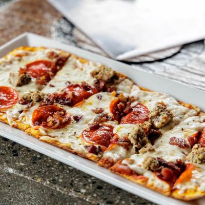 A rectangular pizza with cheese, pepperoni, sausage and bacon bits on a rectangular plate.