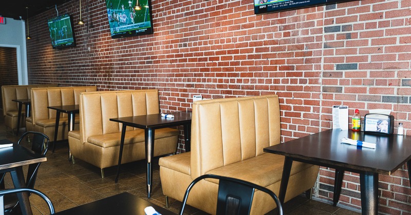 Restaurant interior with booths, brick wall, and televisions displaying a sports game