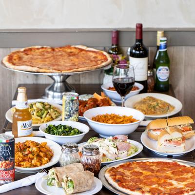 Large table filled with pizzas, pasta dishes, sandwiches, salads, and drinks.