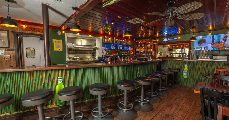 Interior of a bar featuring a long wooden counter, bamboo-style front, lined with black stools