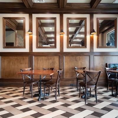 Interior of a dining area with wooden tables, chairs, paneled walls, and a geometric tile floor.