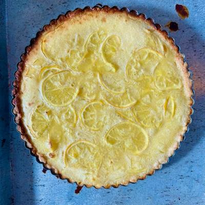 Lemon tart dessert on a baking tray, topped with candied citrus zest.