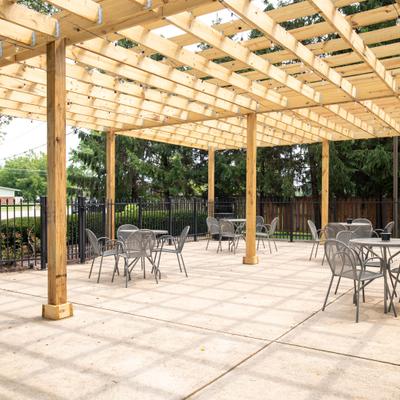 Large wooden pergola covering an outdoor stone patio with several tables and chairs.
