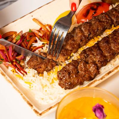 Fork and knife cutting grilled meat skewers over rice with onions.