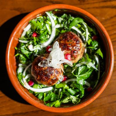 two Georgian 'abkhazura' meatballs in a round clay dish with herbs and onions and pomegranate