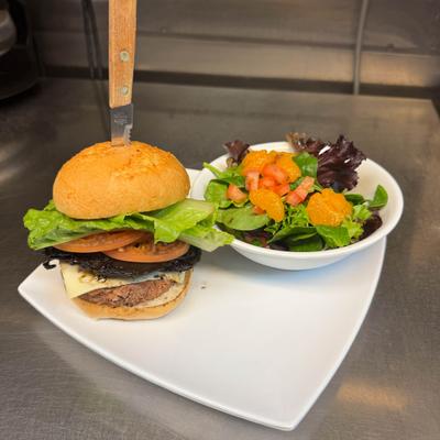 A burger with a mushroom and mixed green salad with mandarin orange and tomato.