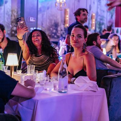 Table of guests smiling while one guest while takes a picture.