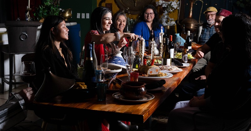 A group of people share food and drinks around a long festive table
