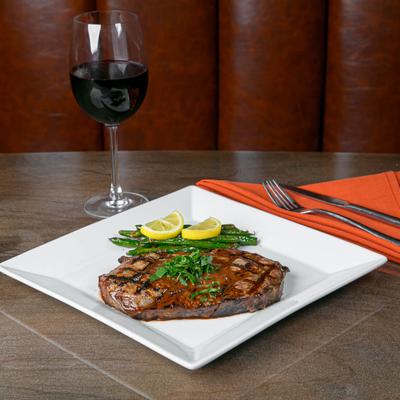 Grilled ribeye steak with green beans and lemon, served with a glass of red wine.