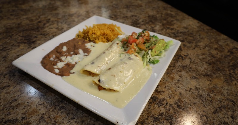 Burritos covered with sauce, served with pico, lettuce, refried beans and rice