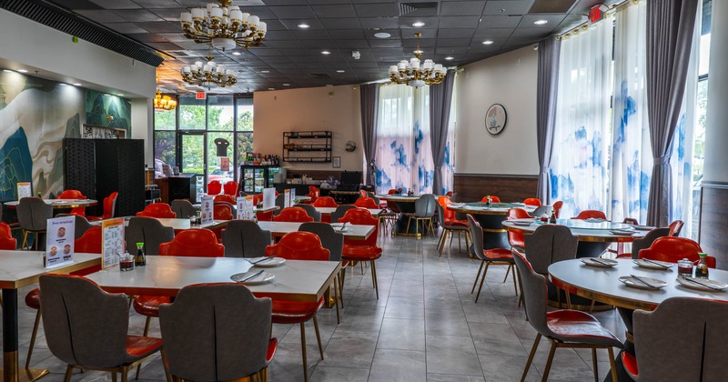 Interior of a restaurant with red chairs, white tables, chandeliers, and blue-patterned curtains