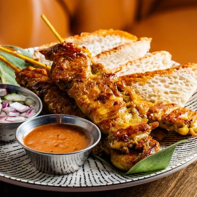 Grilled meat skewers with sliced bread, chopped onions, and a side of dipping sauce.