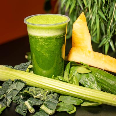 Green Warrior smoothie on a table garnished with spinach, kale, cucumber, and celery.