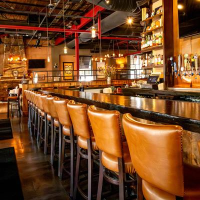 Bar interior with a long dark counter lined by tan leather stools.