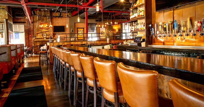 Bar area, long dark wood counter, tan leather bar stools, beer taps, warm lighting