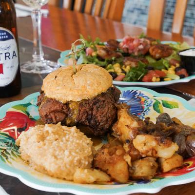 Sweet Heat Fried Chicken Biscuit sandwich with seasoned potatoes and grits, served with a beer.