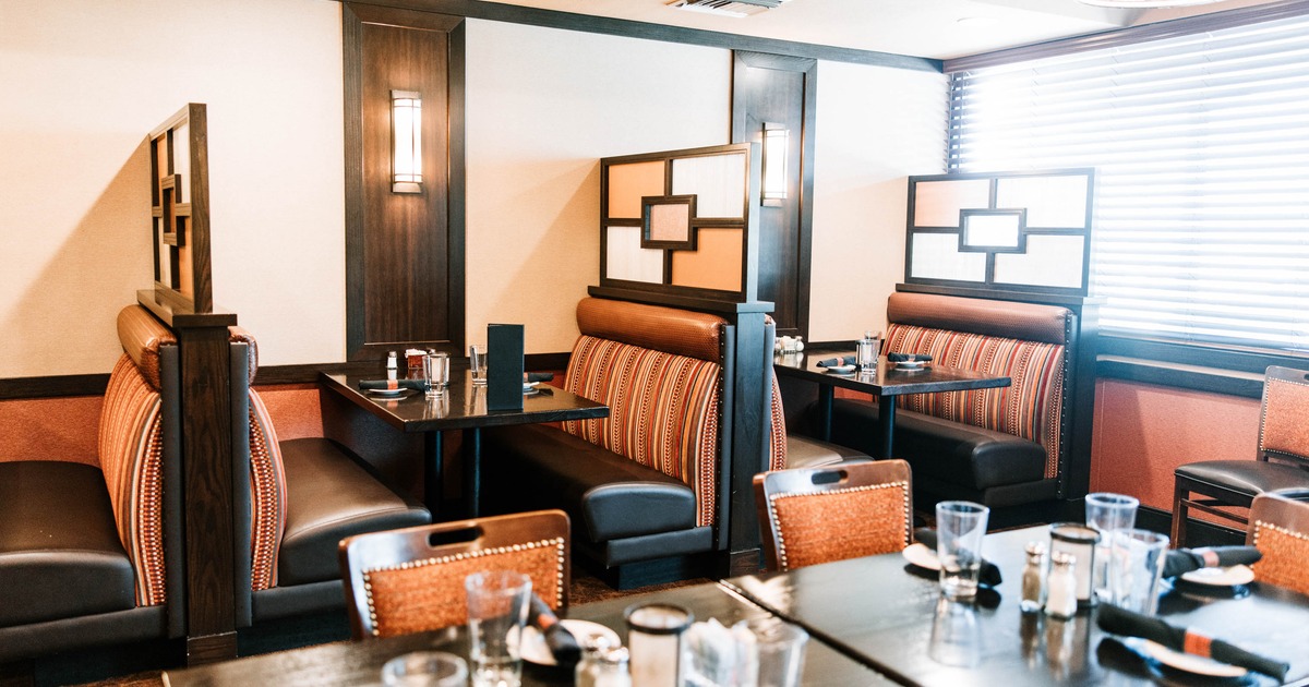 A cozy restaurant interior with booths featuring warm-toned upholstery and dark wooden tables