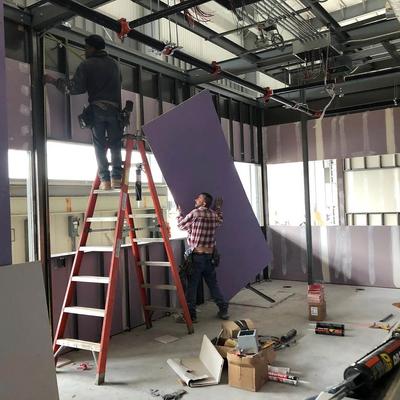 Two construction workers working on a ladder in a room with purple walls