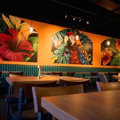 Restaurant interior featuring wooden tables and vibrant tropical flower murals.