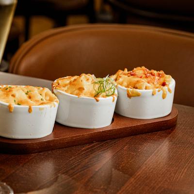 Three small servings of mac and cheese served on a wooden board.
