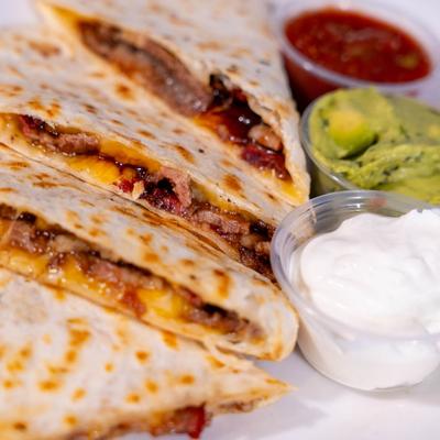 Sliced quesadilla with meat and cheese, served with salsa, sour cream, and guacamole.