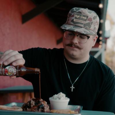Person pouring barbecue sauce over meat and a side dish.
