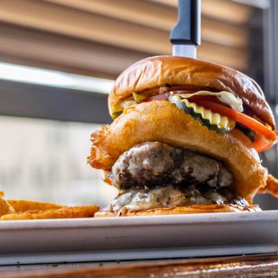A burger topped with cheese, tomato, and a colossal onion ring, served with fries.