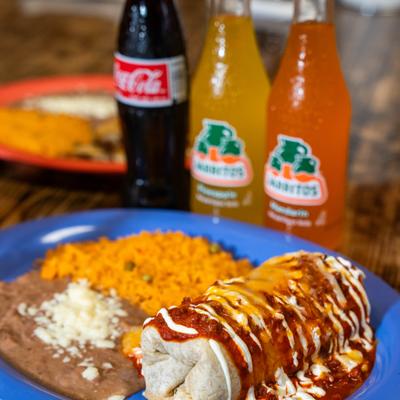 Burrito topped with chili sauce and sour cream, served with rice and beans.
