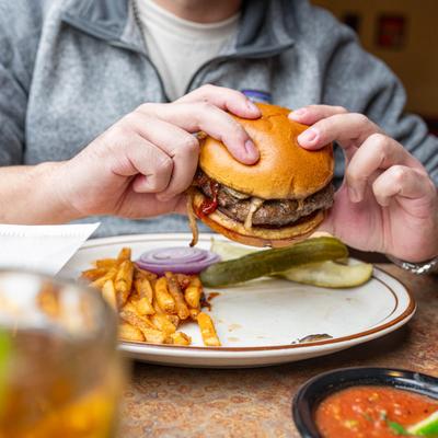 A person lifting a burger from the plate with fries and pickles.