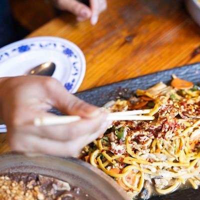 Drunken noodles on a table, a person taking some with chopsticks.