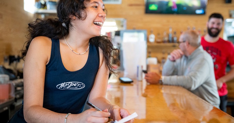 A cheerful employee at a bar writes on a notepad at a bar counter
