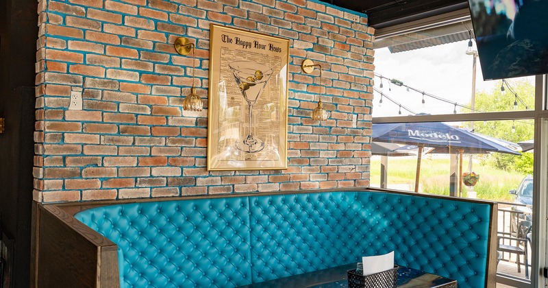 A teal tufted booth sits against a brick wall with martini artwork