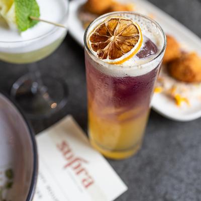 Two-tone red and yellow cocktail on a gray table with Supra menu