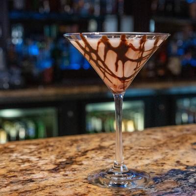 Chocolate Martini glass rests on a a marbled bar top, bar in the background.