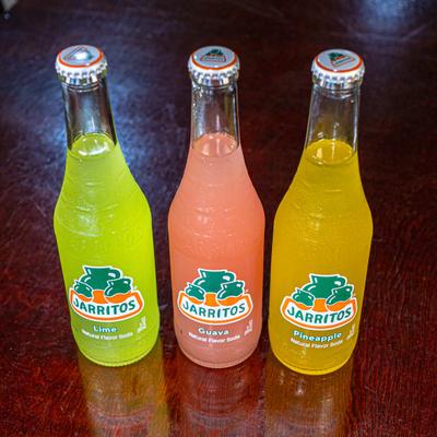 Three glass bottles of Jarritos soda in lime, guava, and pineapple flavors.