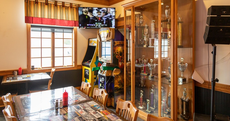 Diner table,  game consoles,  showcase cabinet with awards and trophies, tv screen above