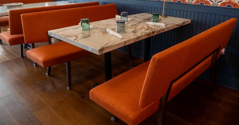 Restaurant interior with orange benches, marble table, and patterned wallpaper