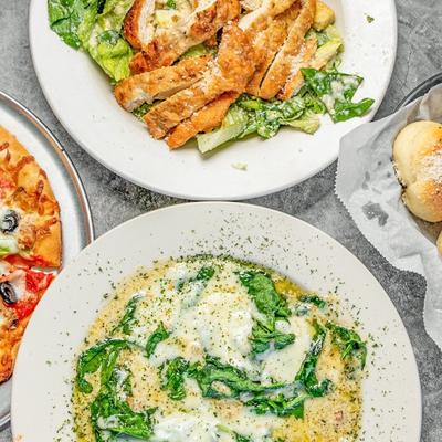A table with Chicken Caesar salad, garlic knots, chicken Florentine, and a pizza.
