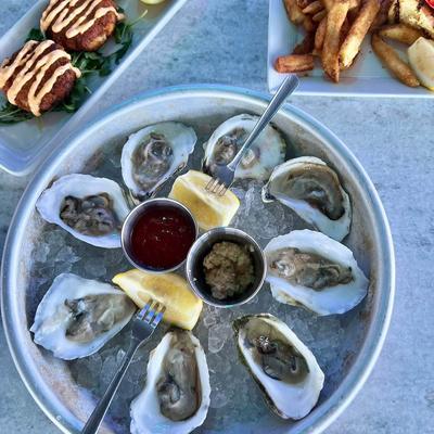 Oysters served on a bed of ice in a metal tray with lemon wedges and sauces.