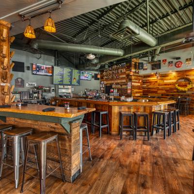 Rstic tavern interior featuring an expansive wooden bar, stools, and wood-paneled walls.