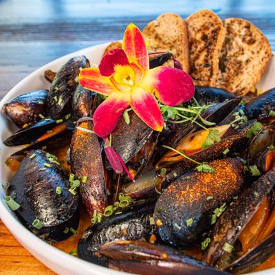 Mussels in tomato-based sauce, served with toasted bread and a flower garnish.