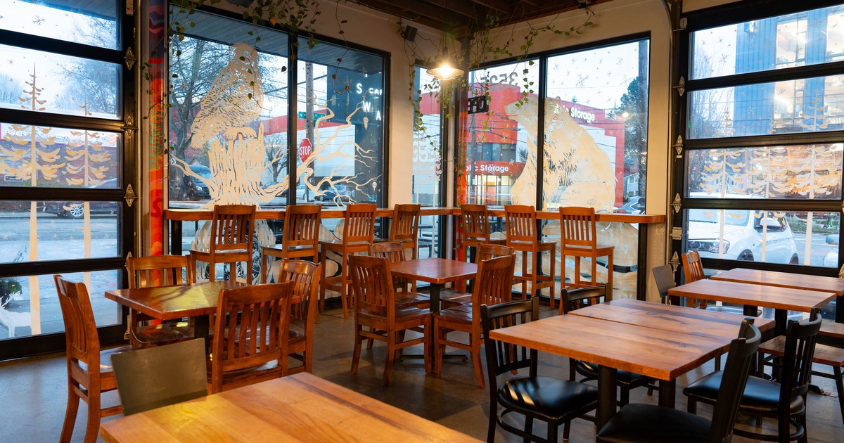 Interior of a café with wooden tables, chairs, and large decorated windows